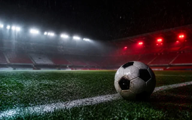 Fußball Wetten Tipps: Ball auf nassem Rasen im Flutlicht bei Regen