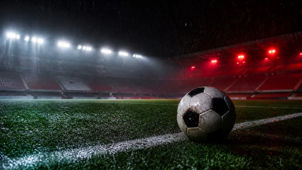 Fußball Wetten Tipps: Ball auf nassem Rasen im Flutlicht bei Regen